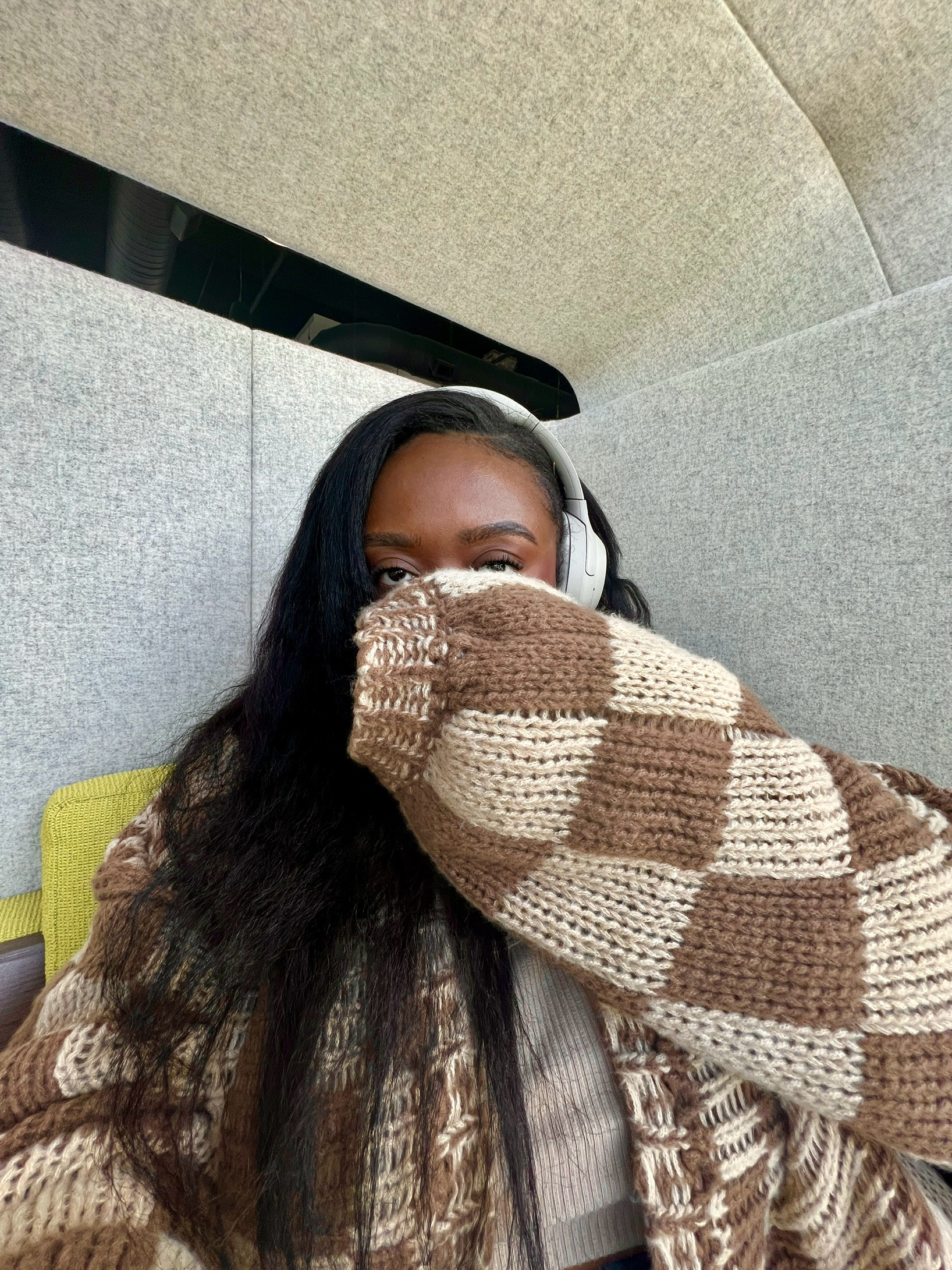 Girl wearing headphones covering her face with her sweater.