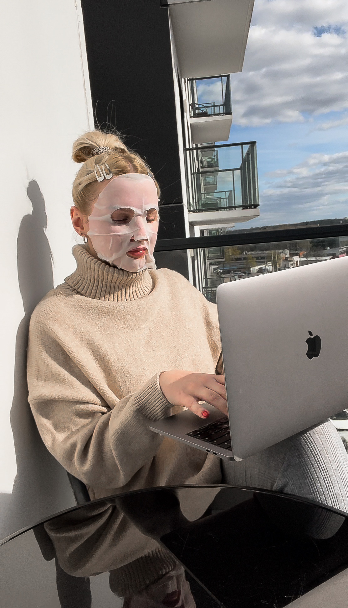 Woman on her computer outside with a face mask on.