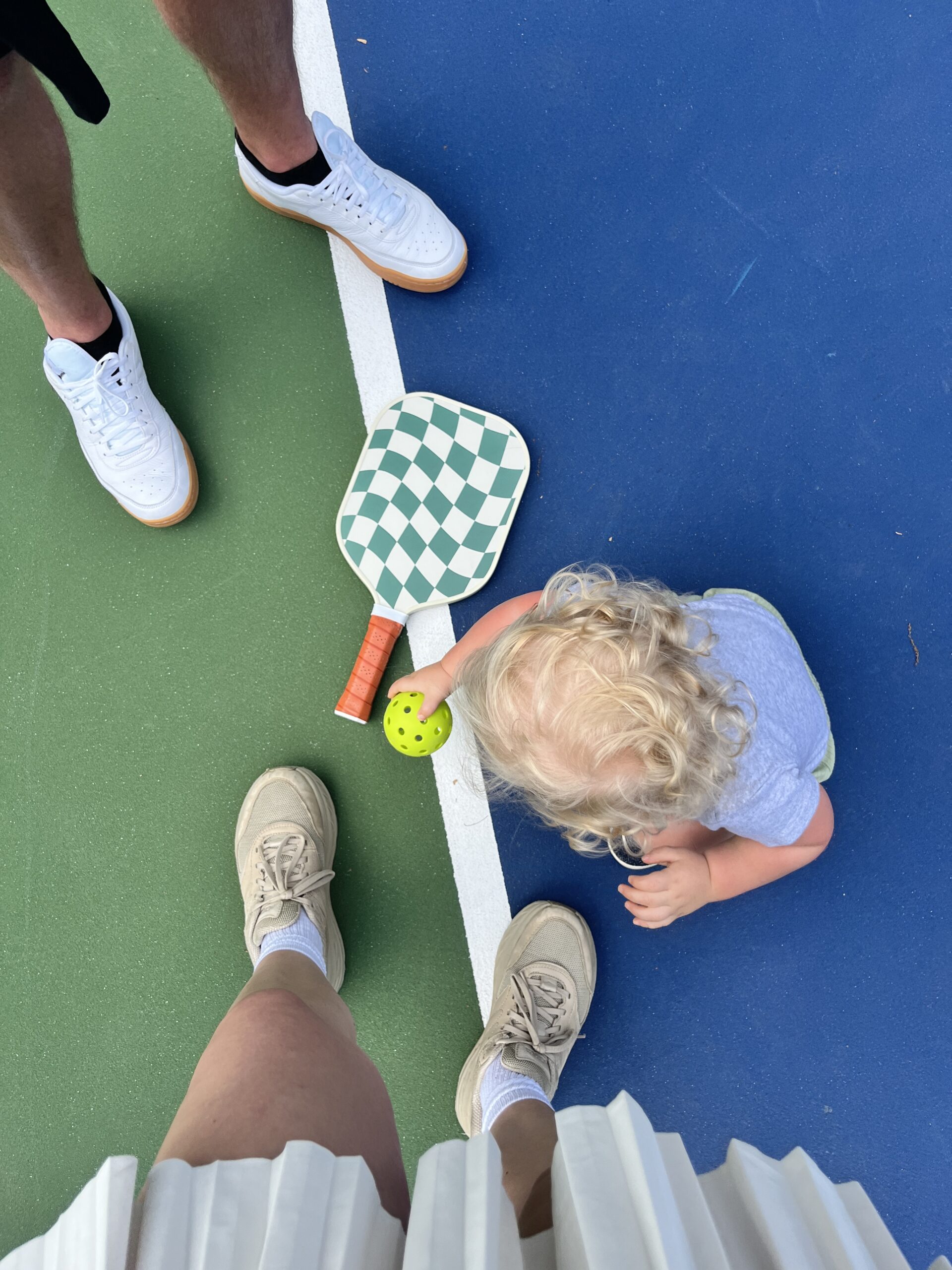 Toddler playing pickleball with parents.
