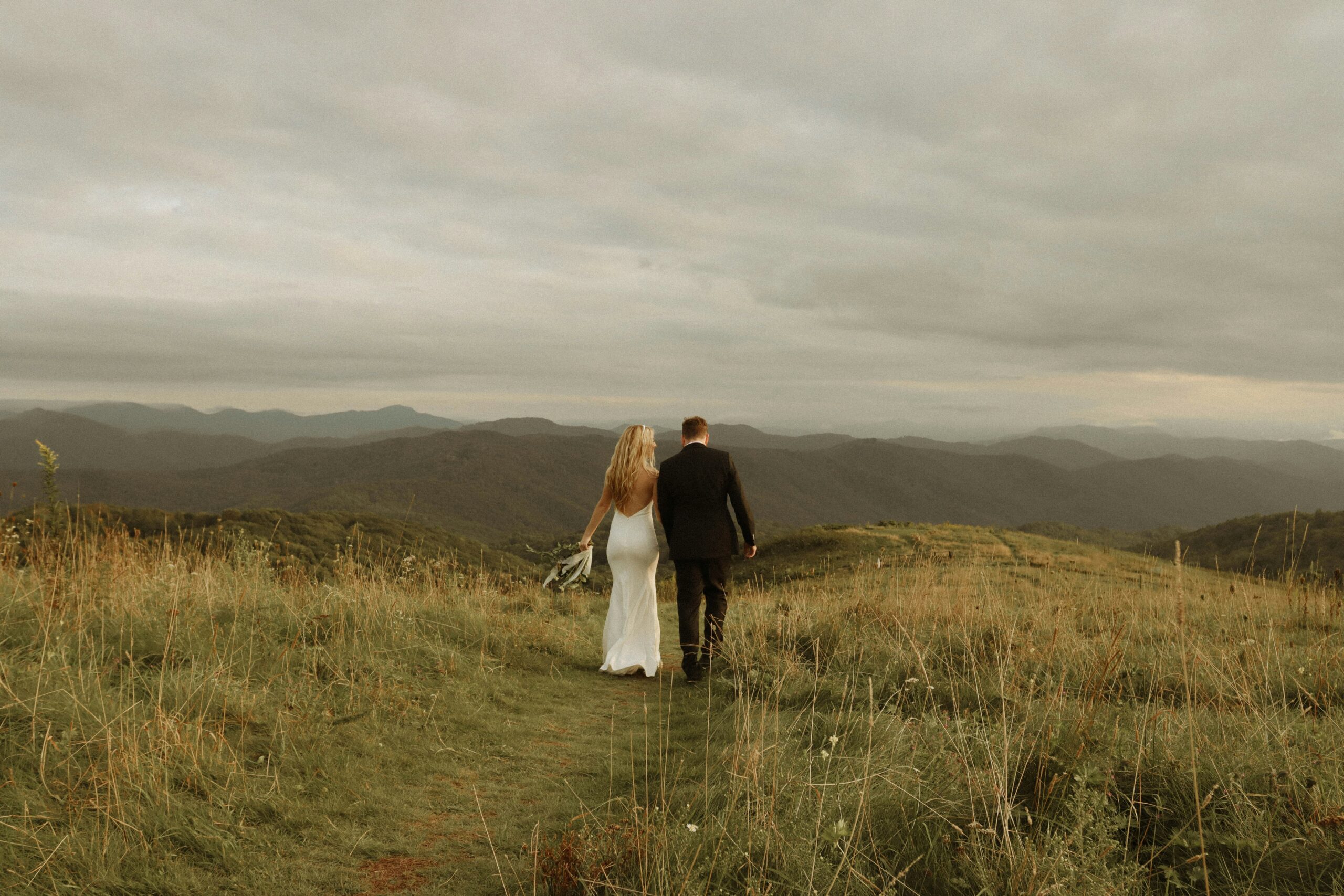 Bride and groom walking away in the grass.