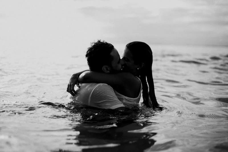 Black and white image of couple kissing in the ocean.