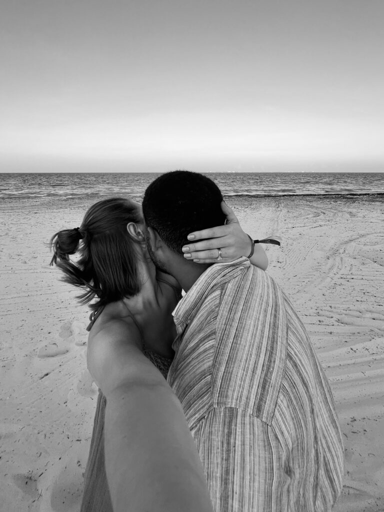 Black and white image of couple on beach, boy kissing girl's cheek.