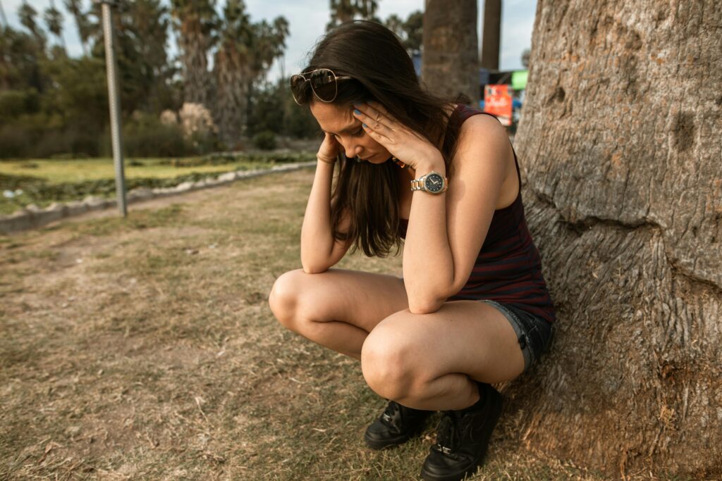 Girl stressed, holding her head in her hands, sitting on a tree.