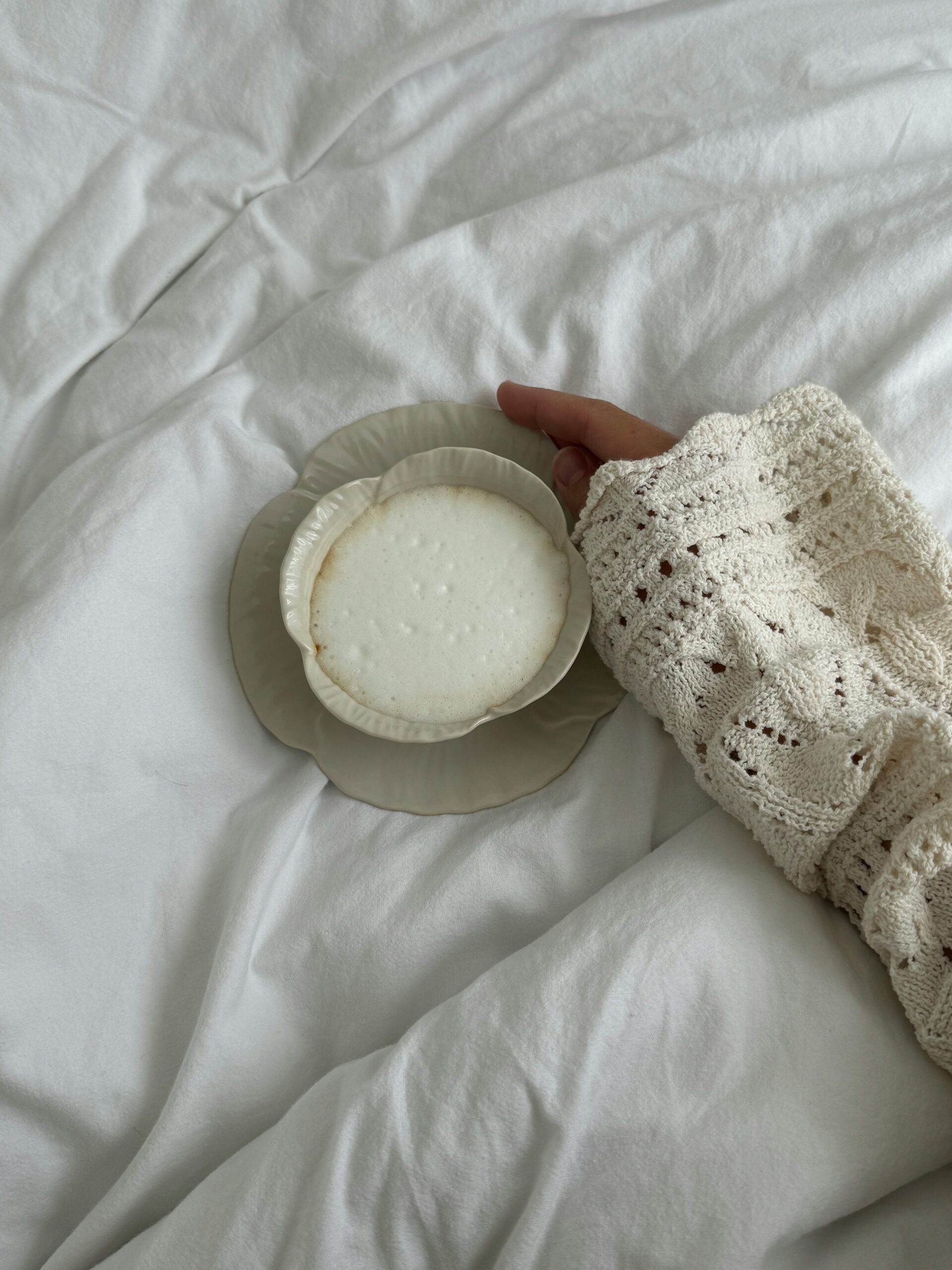 Girl holding hot cup of coffee on her bed.