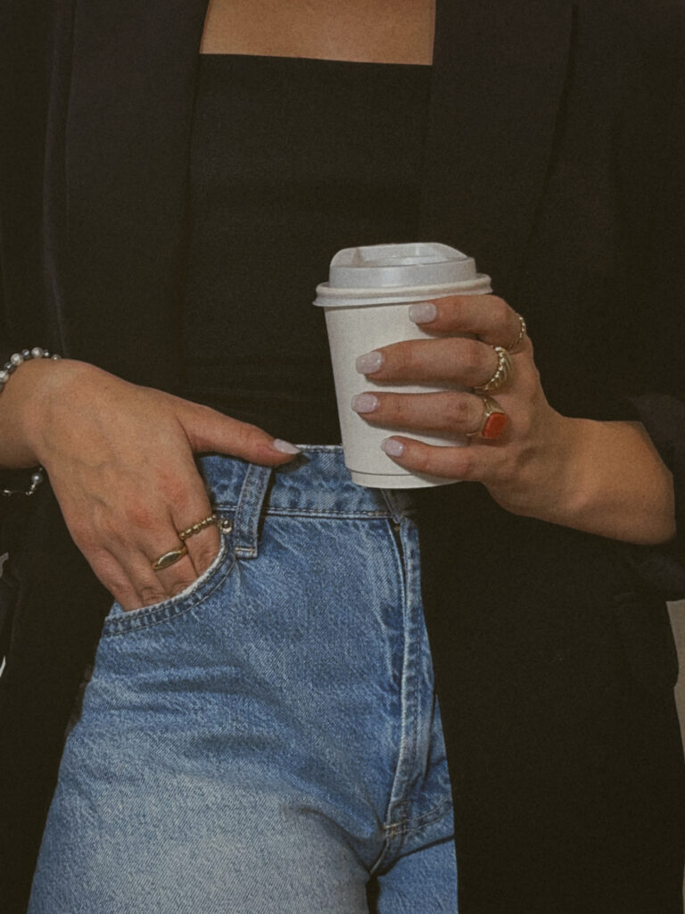 Woman holding coffee in one hand and other hand in her jean pocket.