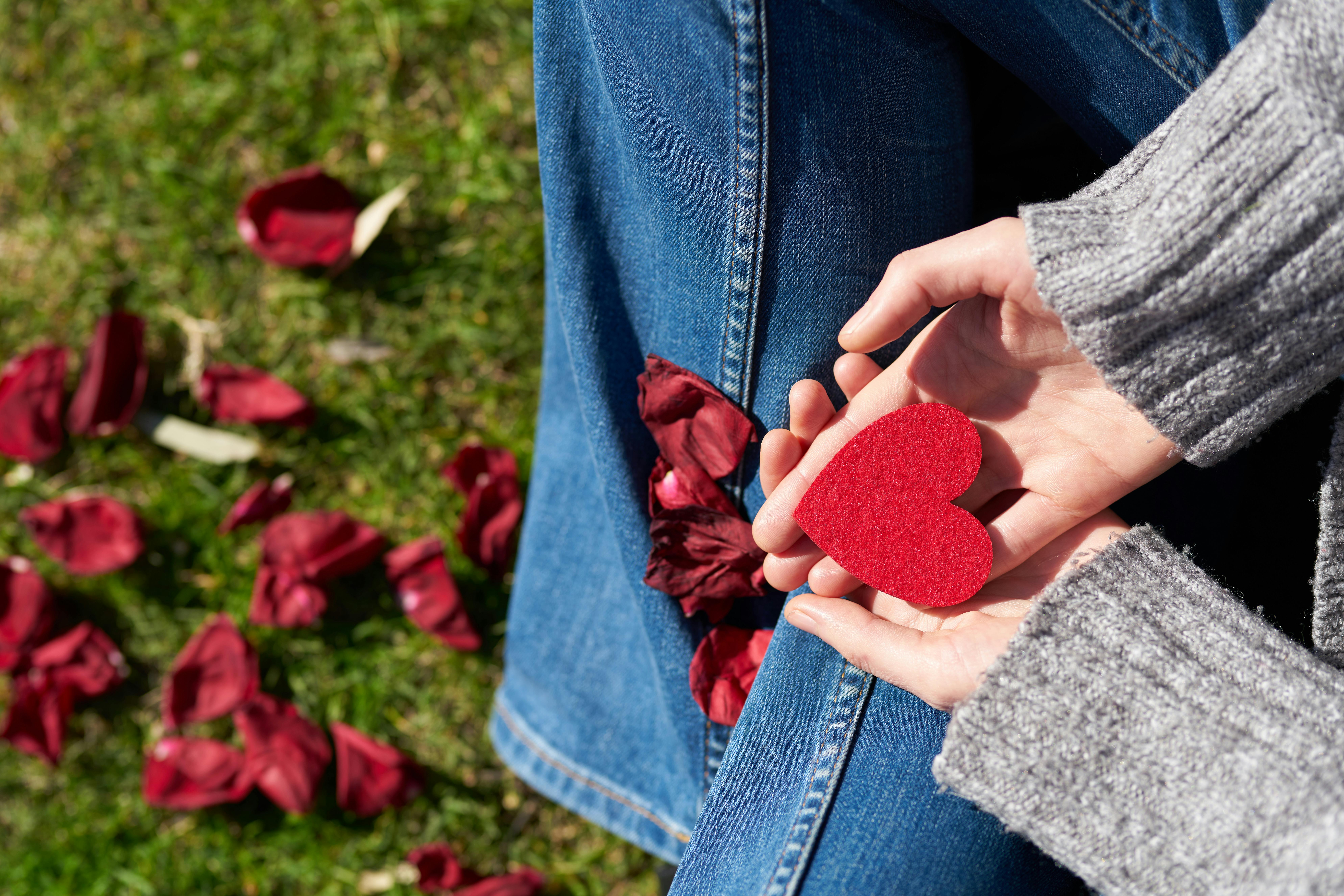Woman holding a red heart in her hands in her lap.