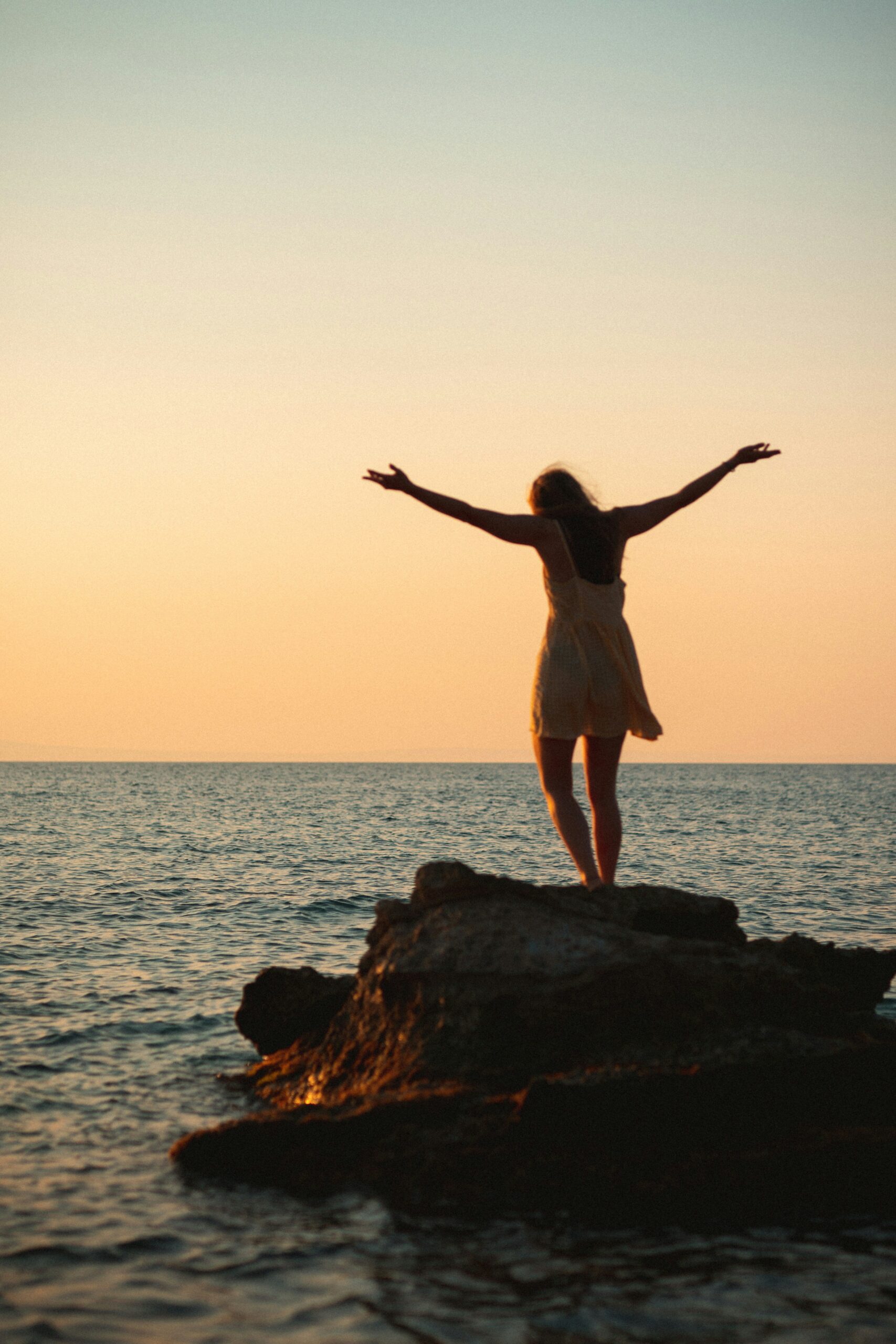 Free spirited woman on the rocks at beach during sunset.