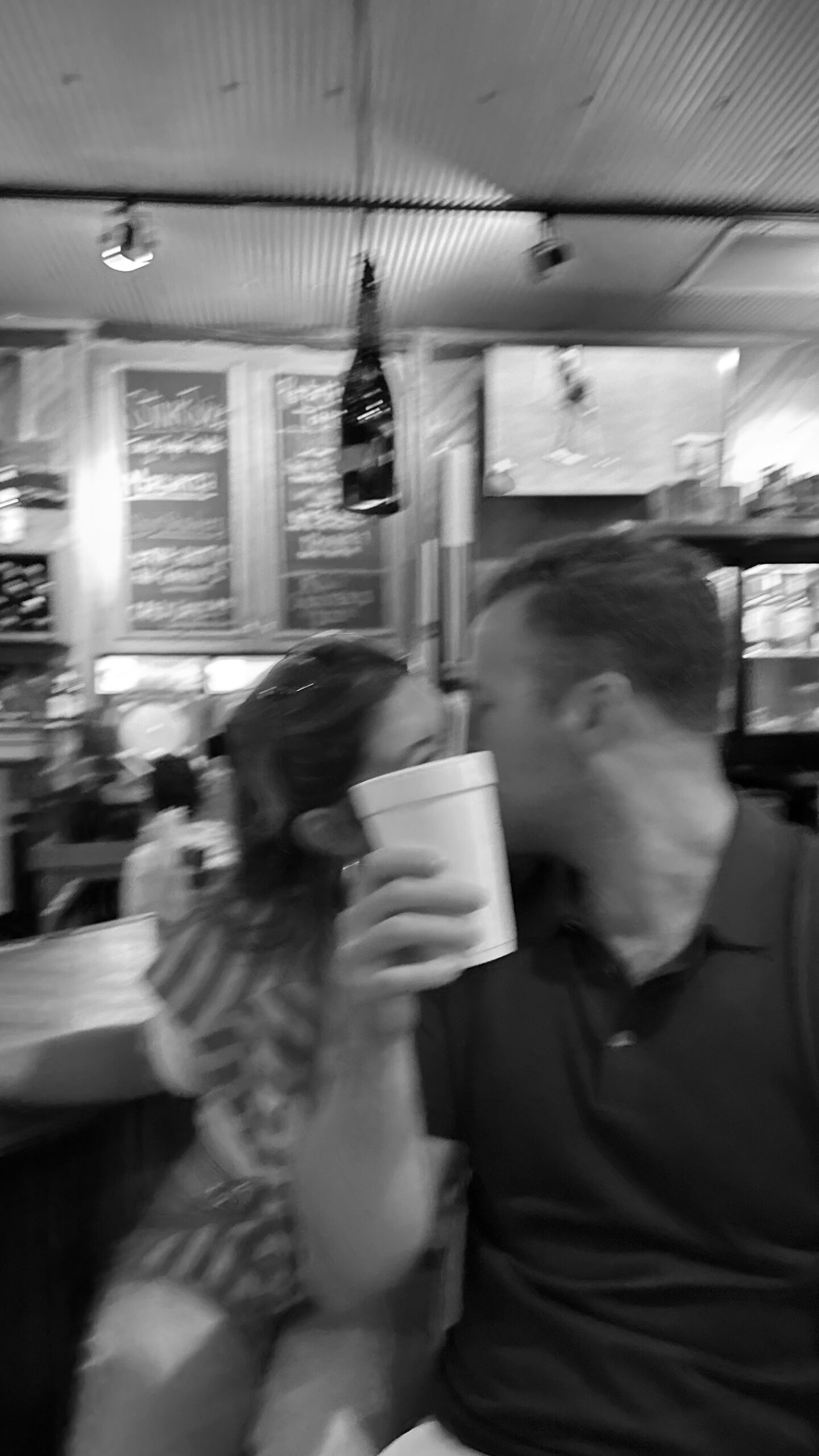 Black and white picture of couple kissing and cup in front of them.