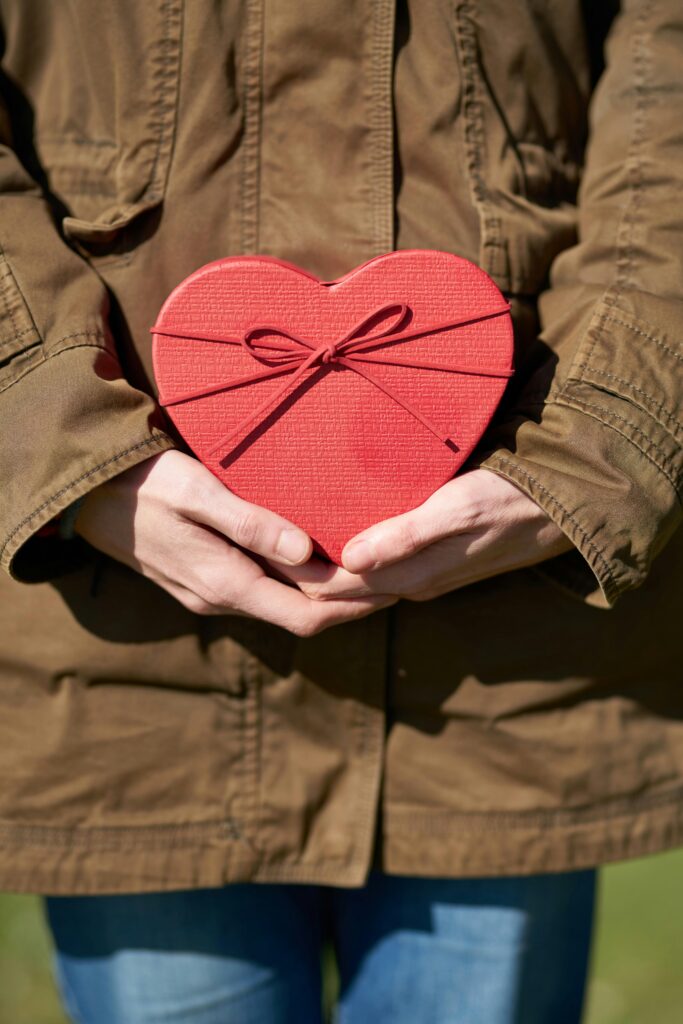 Person holding a red heart chocolate box in her hands.
