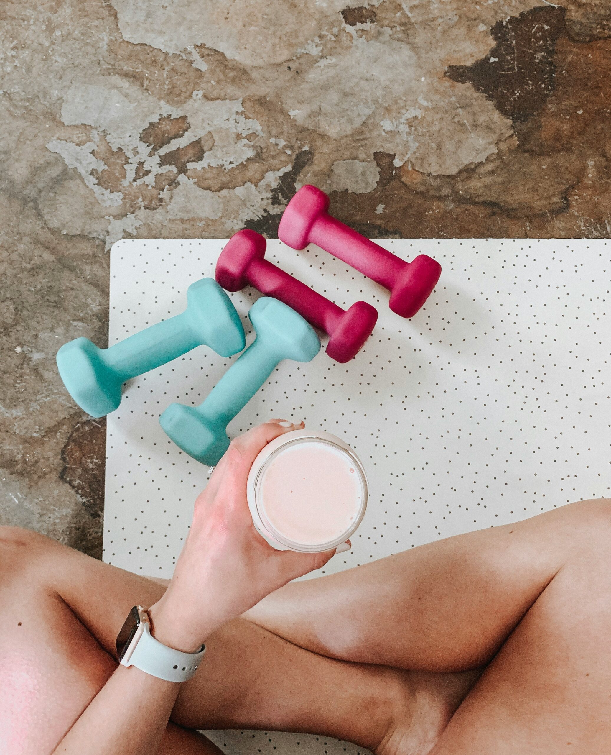 weights on yoga mat while woman holds protein shake drink