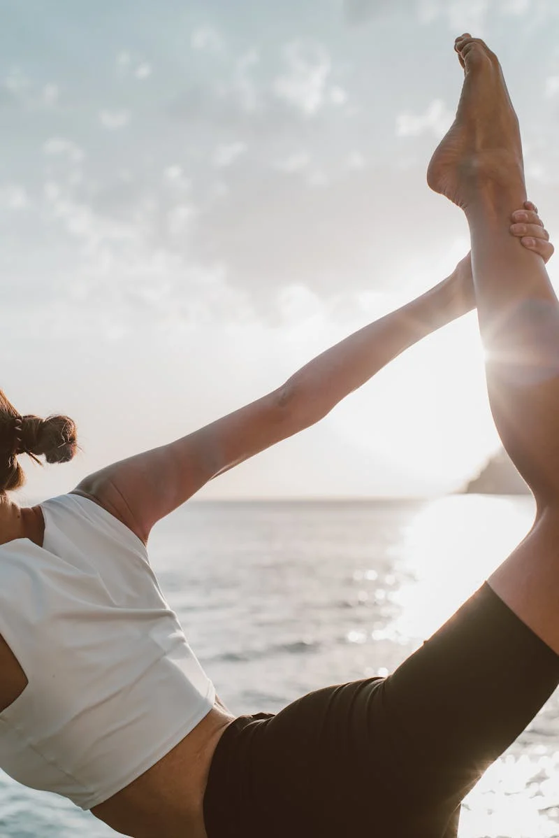 Woman doing yoga by the water outside.