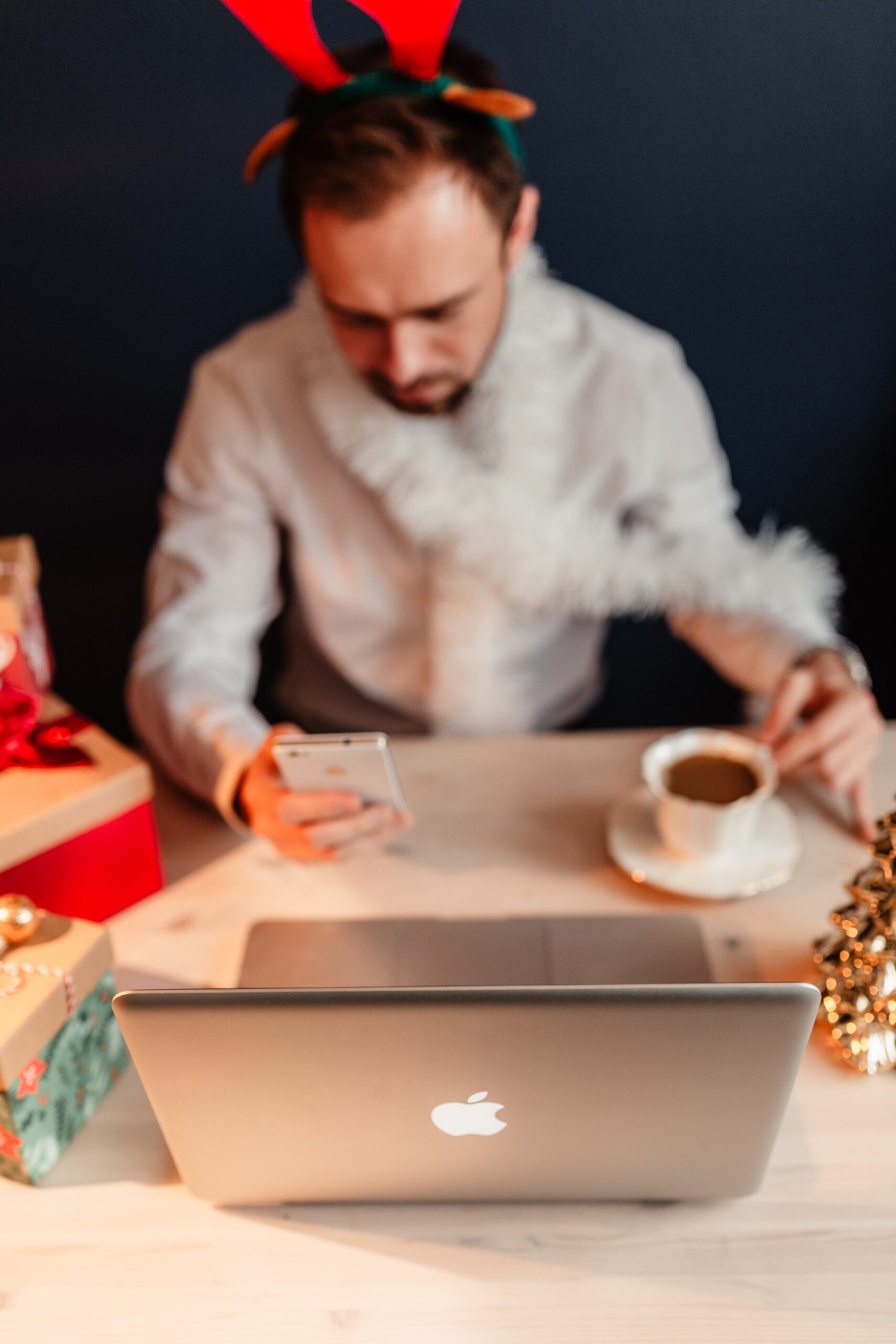 Man looking at his phone, in front of computer, with holiday decorations.