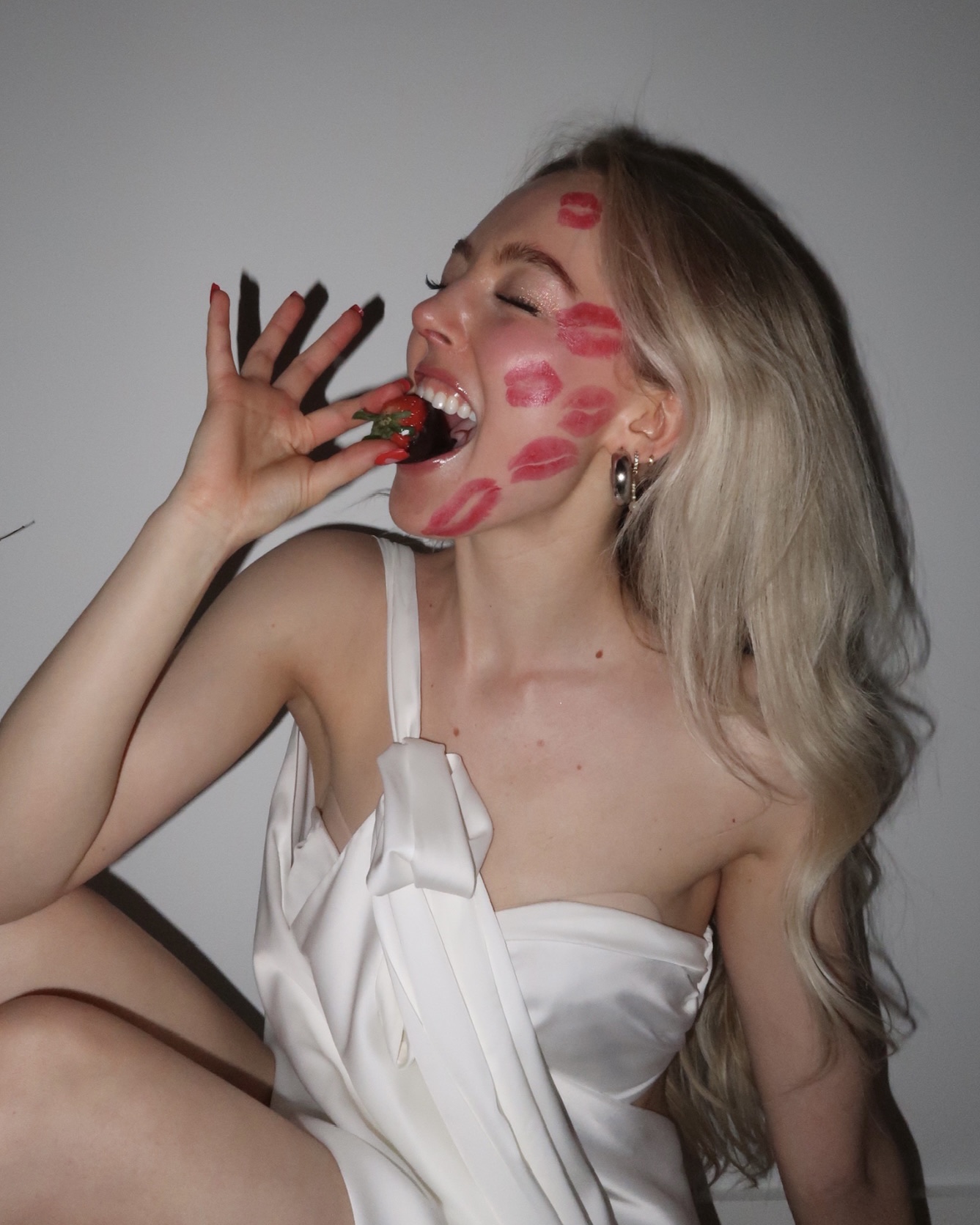 Single girl with kiss marks on her face biting a strawberry, celebrating valentine's alone and contented in New York