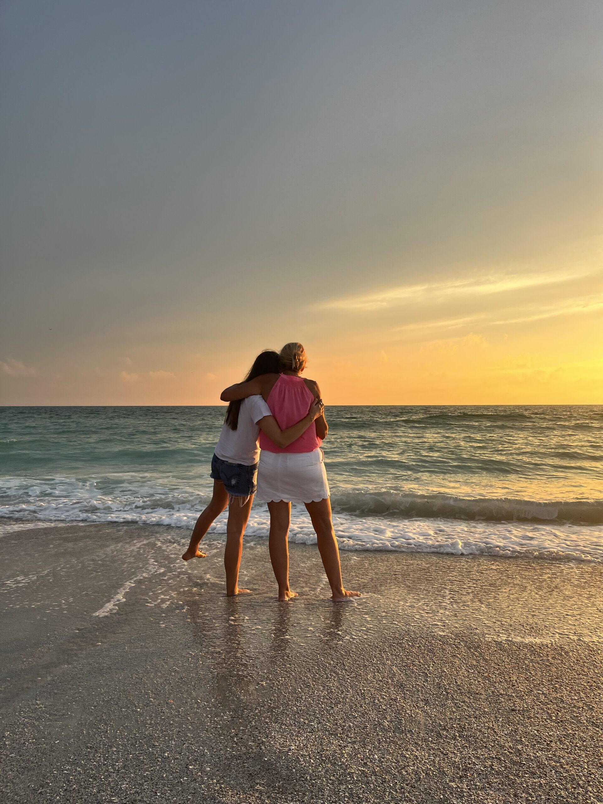 Mother and daughter hugging each other watching the sunset together on the beach in Brooklyn