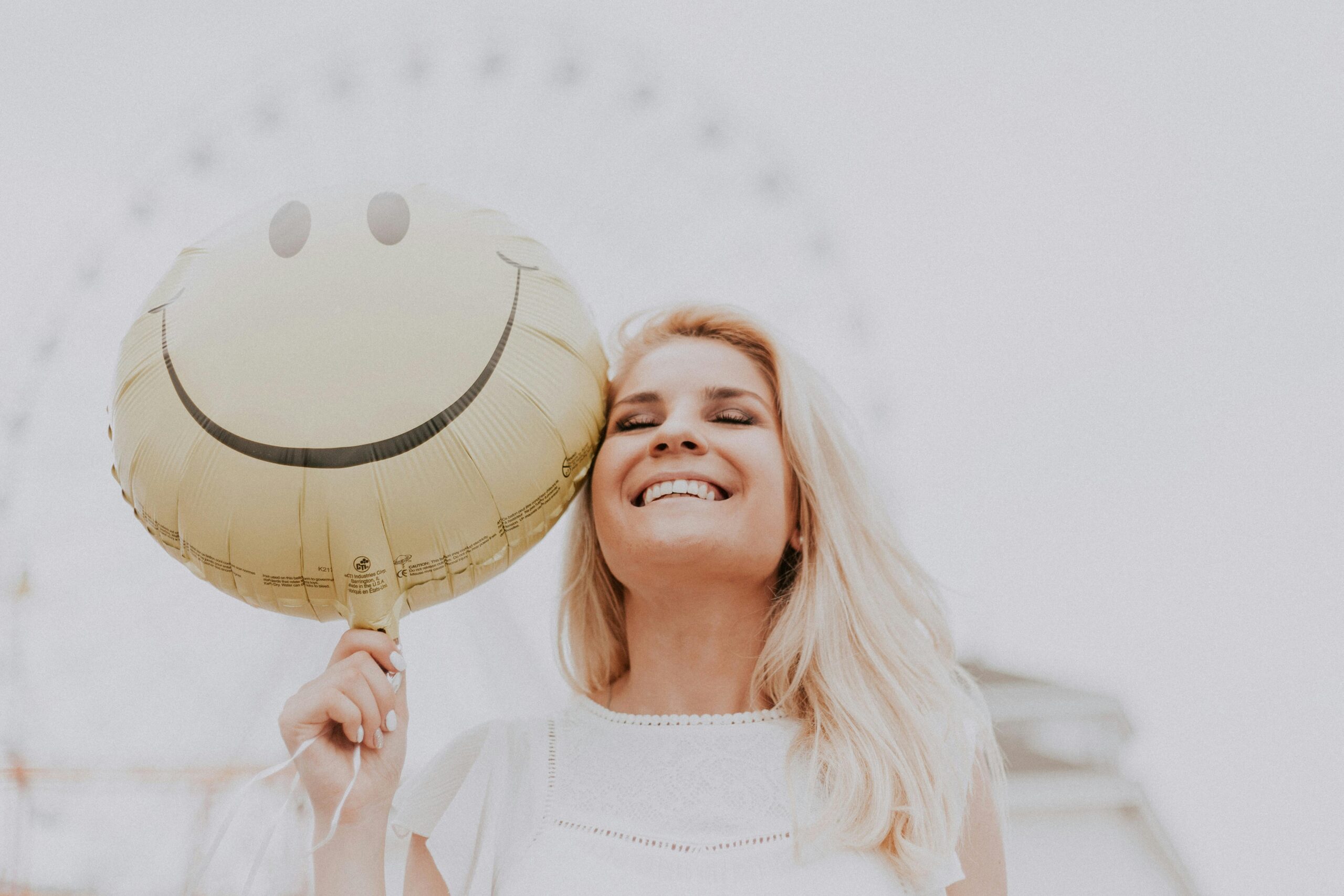 Woman holding a balloon with a happy face design in Manhattan while smiling.
