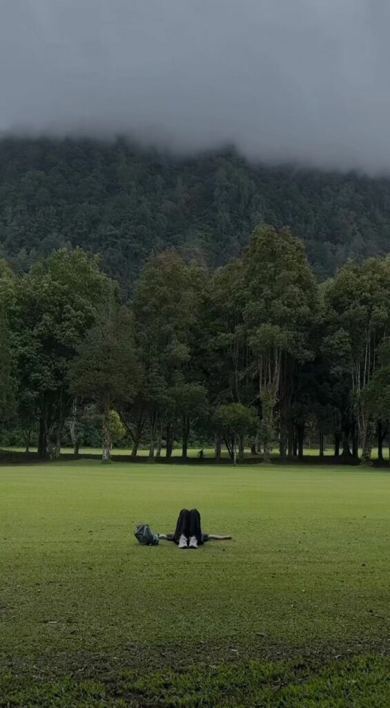 A person lying down in the middle of the field trying to relax at Manhattan 