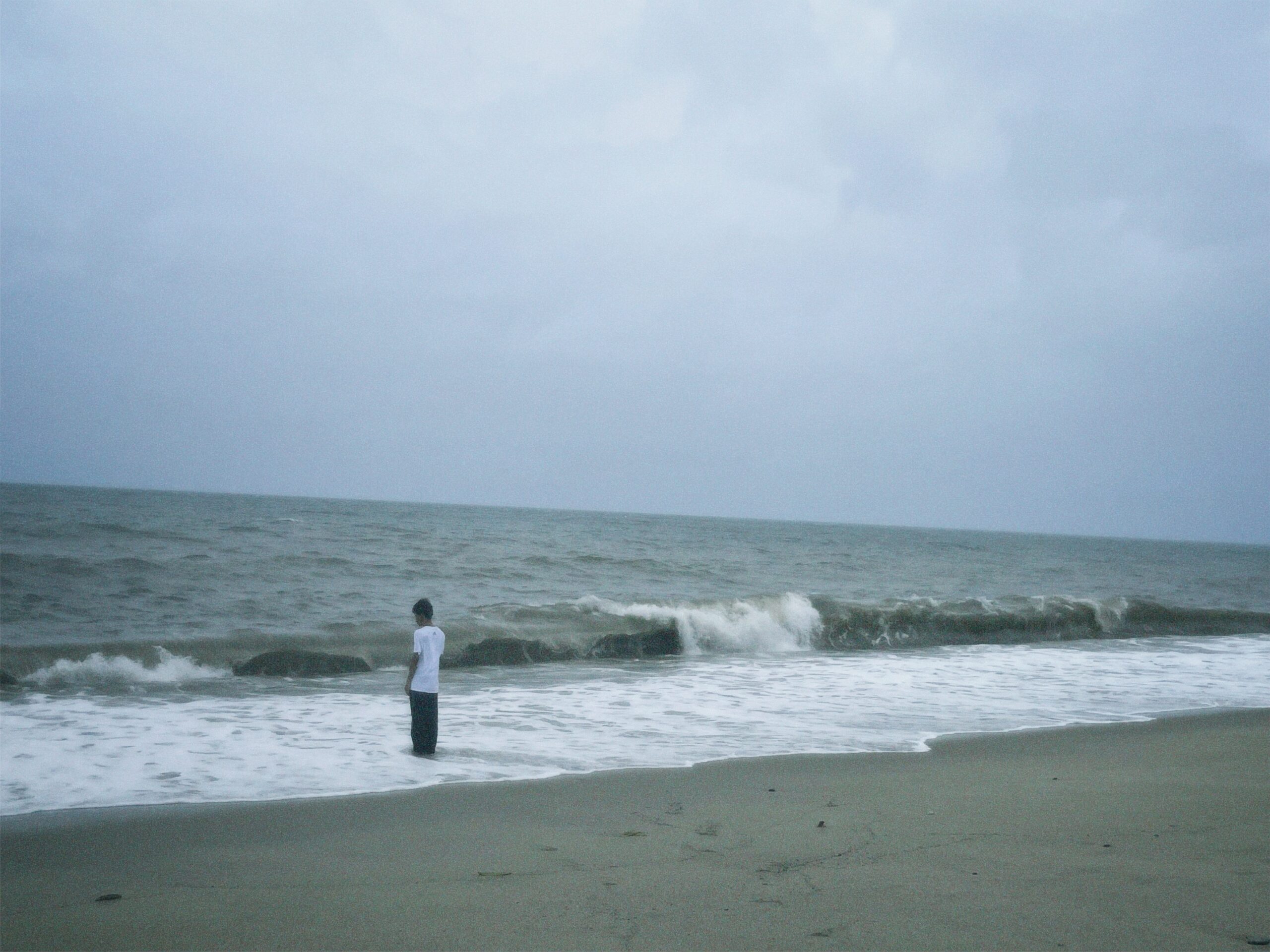 A man standing alone near the waves feeling emotionally numb at Manhattan